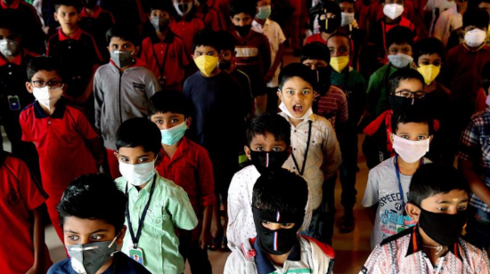 En India, niños hacen una formación con mascarillas para evitar contagios por coronavirus.