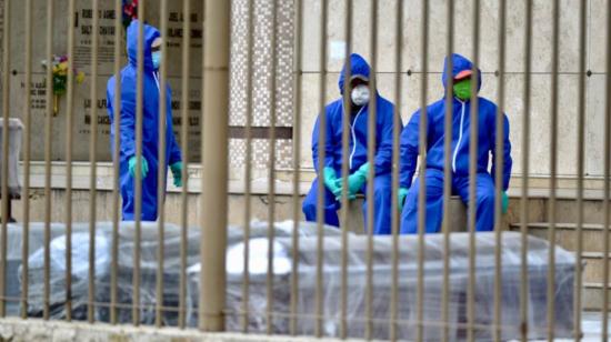 Ciudadanos con trajes de protección descansan junto a un grupo de ataúdes en un camposanto de Guayaquil, el 1 de abril de 2020.