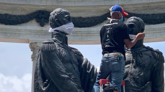 Un trabajador municipal coloca las mascarillas a las estatutas de Simón Bolívar y José de San Martín, en Guayaquil.