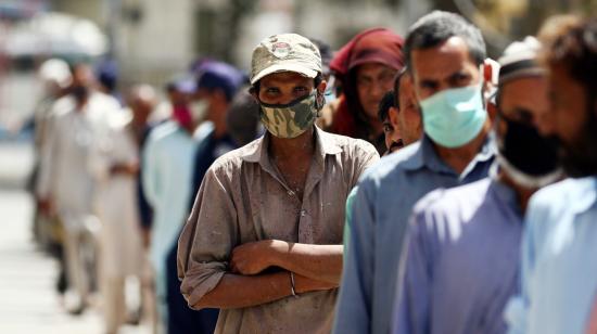 Los casos de Covid-19 siguen aumentando. Decenas de personas protegidas con mascarillas esperan su tuno para recibir comida en Karachi, Pakistán.