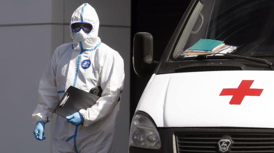 Personal médico con su traje de bioseguridad, mascarilla y guantes a lado de una ambulancia.