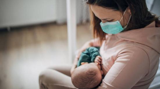 Mujer con mascarilla dando de lactar a su hijo.