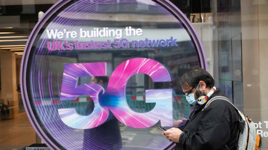 Persona revisa su teléfono afuera de una tienda móvil que muestra un letrero 5G, Oxford Street, Londres, el 12 de junio de 2020.