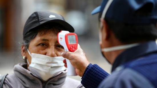 Una mujer con una máscara mientras el personal de seguridad le toma la temperatura antes de abordar un transporte público, este miércoles 10 de junio de 2020 en una calle de Quito, Ecuador.