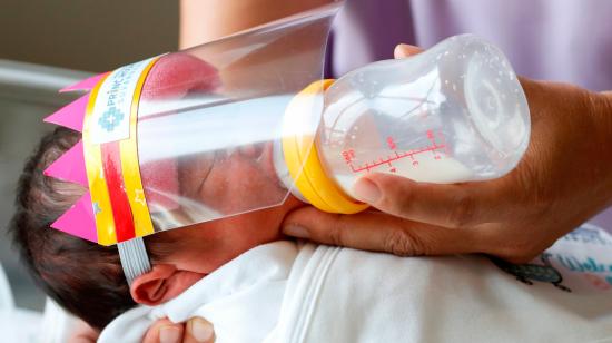 Imagen referencial de un bebé recién nacido tomando su biberón protegido por un visor de plástico.