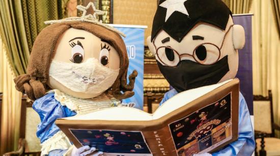 Juanita y Juan Pueblo, con mascarillas, sostienen un libro en medio del acto de presentación de la Feria Internacional del Libro de Guayaquil del 2020.