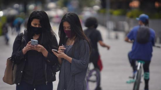 Dos mujeres miran sus celulares el 18 de septiembre de 2020 en la avenida Naciones Unidas, en el norte de Quito.