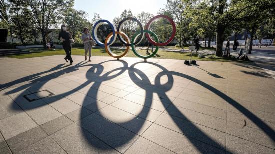 Personas caminan junto al monumento de los anillos olímpicos, en las inmediaciones del Estadio Olímpico de Tokio, el domingo 23 de mayo de 2021.