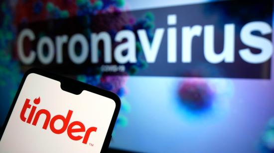 El logotipo de la aplicación de citas Tinder que se muestra en un teléfono móvil con un modelo ilustrativo de coronavirus en un monitor de fondo.