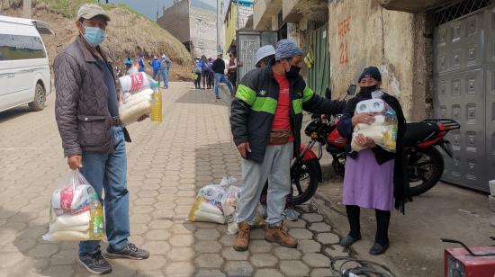 Ricardo Maila (centro) entrega una funda de alimentos a una moradora de La Comuna, el 16 de febrero de 2022.