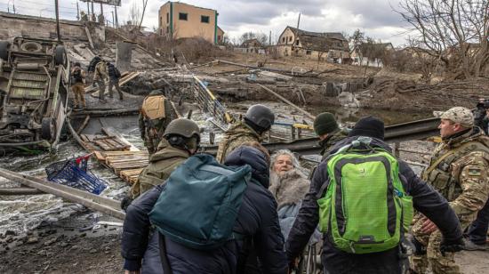 Miembros del ejército ucraniano llevan a una anciana en silla de ruedas para cruzar el puente destruido, mientras la gente huye de la ciudad de primera línea de Irpin, región de Kiev, en Ucrania, el 7 de marzo de 2022.