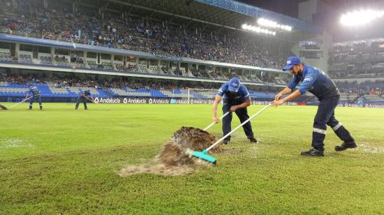 Personal de Emelec intenta retirar el agua acumulada en la cancha por la fuerte lluvia que cae en Guayaquil, el 20 de marzo de 2022.