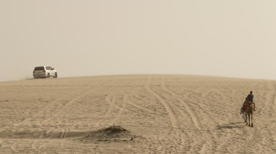 Un turista en camello y un carro todoterreno se adentran en el desierto de Qatar.