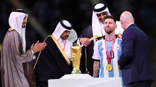 El príncipe Jassim bin Hamad bin Khalifa Al Thani aplaude mientras el emir de Qatar, el jeque Tamim bin Hamad Al Thani, le pone un Bisht a Lionel Messi de Argentina junto al presidente de la FIFA, Gianni Infantino durante la ceremonia de entrega de premios de la final del Mundial.