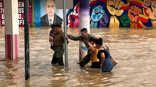 Personal del Ejército ayuda a varias personas a cruzar por una calle inundada en Chone, el 8 de marzo de 2023. 