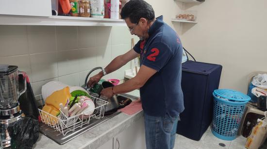 Un hombre intenta lavar sus platos en su casa, ubicada en Turubamba.