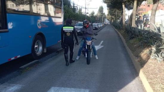 Un agente de tránsito sanciona a un conductor de una motocicleta por invadIr el carril exclusivo del Trolebús, el 21 de julio de 2023