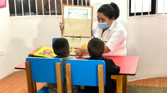 Una cuidadora de un centro infantil de Quito enseña a dos niños, en 2022.