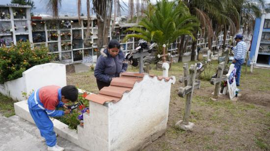 Dos personas arreglan la tumba de un ser querido en un cementerio de Quito, el 2 de noviembre de 2023.