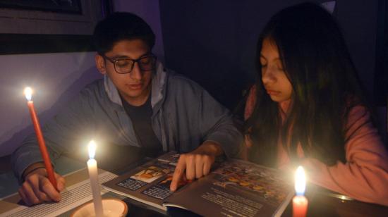 Renata y Daniel Barros estudiando con velas por el corte de energía eléctrica en Cuenca, el 27 de octubre de 2023. 