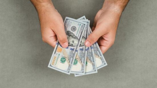 Imagen referencial de una persona con billetes de dólares en sus manos. 