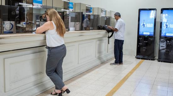 Dos personas en las ventanillas de atención para el pago de impuesto predial en Guayaquil. 