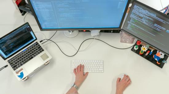Imagen referencial de un profesional tecnológico junto a tres pantallas de computadores. 