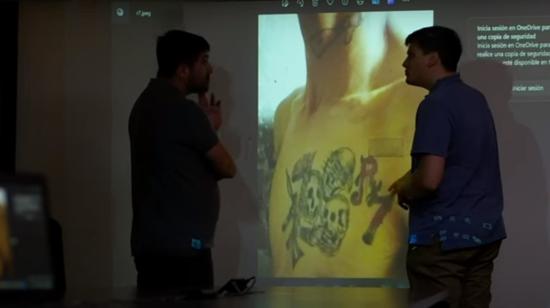 Dos periodistas del canal Mega junto a la fotografía de un detenido ecuatoriano, que tiene un tatuaje alusivo a la banda R7.