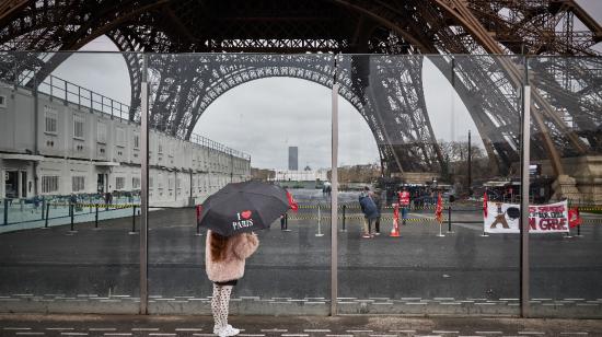 Un peatón con un paraguas que dice "Amo París" mira junto a la Torre Eiffel y una pancarta (R) que dice "empleados de la Torre Eiffel en huelga" en París el 19 de febrero de 2024.