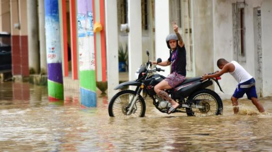 Un hombre empuja la moto de un ciudadano en Chone, ciudad de Manabí afectada por las inundaciones, el 21 de febrero de 2024.