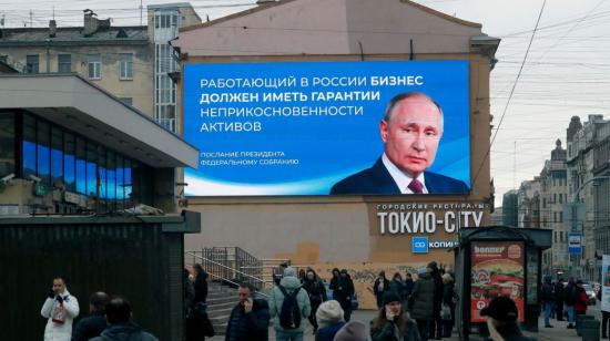 La gente pasa junto a un enorme cartel digital que muestra al presidente y candidato presidencial ruso Vladimir Putin, en San Petersburgo, Rusia, el 14 de marzo de 2024.