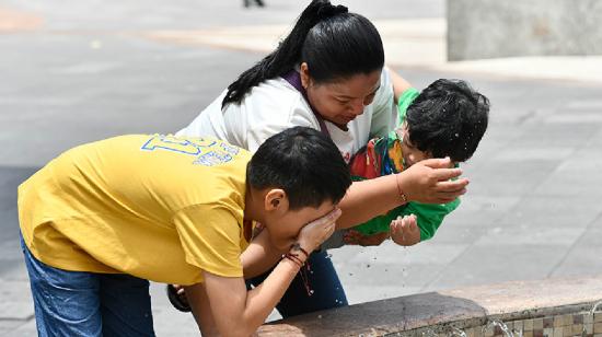 Una mujer y sus hijos en una fuente de agua en el centro de Guayaquil.