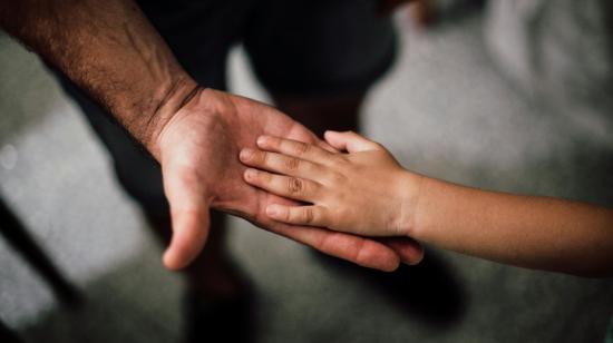 Imagen referencial de la mano de un padre junto a su hijo.