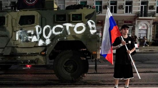 A man holds the Russian national flag in front of a Wagner group military vehicle with the sign read as "Rostov" in Rostov-on-Don late on June 24, 2023. - Rebel mercenary leader Yevgeny Prigozhin who sent his fighters to topple the military leaders in Moscow will leave for Belarus and a criminal case against him will be dropped as part of a deal to avoid "bloodshed," the Kremlin said on June 24. (Photo by STRINGER / AFP)