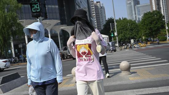 Las personas que se cubren la cabeza para protegerse del sol cruzan la calle durante las condiciones de la ola de calor en Beijing el 19 de julio de 2023. 