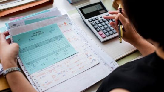 Imagen referencial de una persona revisando facturas y realizando cálculos con una calculadora. 