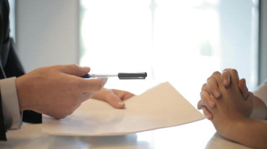 Fotografía referencial de un ejecutivo presentando un papel a un cliente para ser firmado.