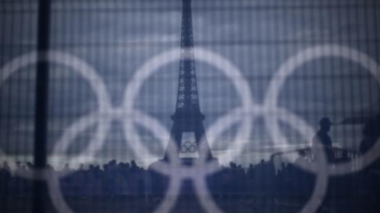 Los visitantes pasan junto a una pancarta con anillos olímpicos colocada sobre una barrera con la Torre Eiffel al fondo, el 16 de julio de 2024.