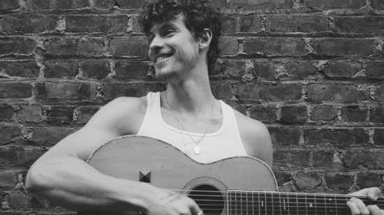 Shawn Mendes sonriendo mientras sostiene una guitarra