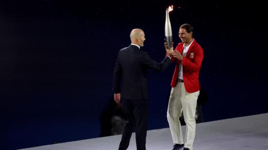 El tenista español Rafa Nadal (d) recoge la antorcha olímpica de manos del exfutbolista Zinedine Zidane en la Plaza del Trocadero durante la ceremonia de inauguración de los Juegos Olímpicos de París 2024.