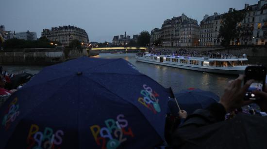 Miembros del público se protegen de la lluvia con paraguas mientras observan el desfile de las delegaciones por el río Sena.