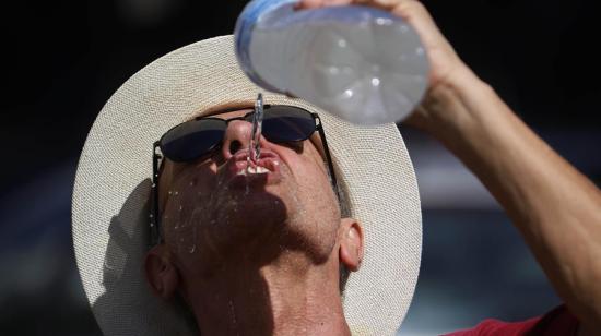 Un hombre se refresca con agua de una botella mientras camina por el Puente Romano de Córdoba, 9 de agosto de 2024.