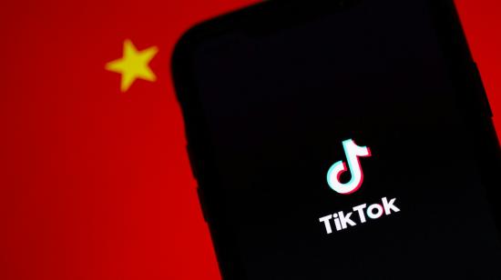 Fotografía referencial de un celular con el logo de TikTok en su pantalla mientras en el fondo se ve parte de una bandera china.