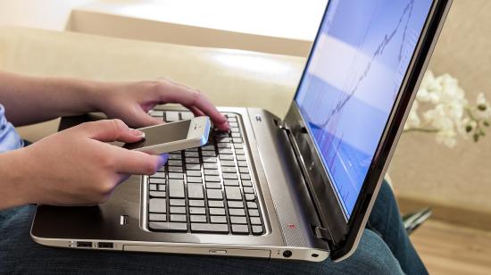 Una persona con una laptop en sus piernas y un celular en la mano. Imagen referencial.