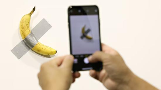 Una persona tomando foto al plátano pegado en la pared.