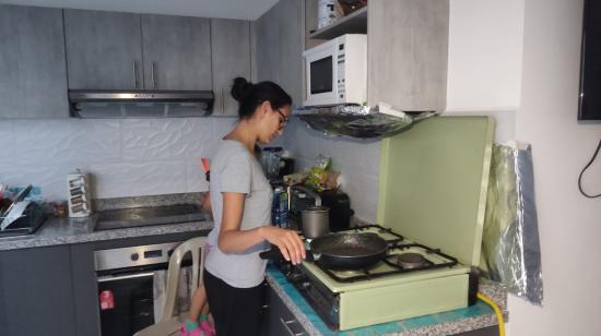 Una mujer prepara sus alimentos en una cocineta a gas. A sus espaldas una cocina de inducción apagada por los cortes de luz.