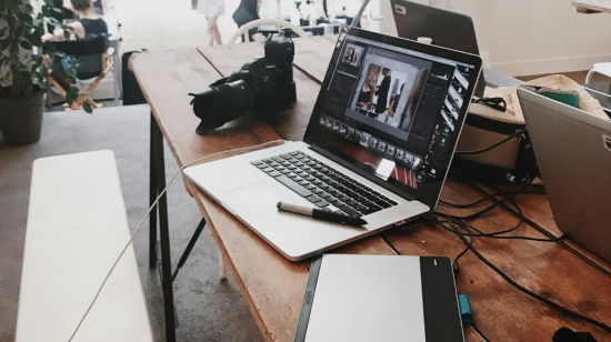 Fotografía referencial de distintos dispositivos tecnológicos como laptops, cámaras y tabletas graficadoras en una mesa.