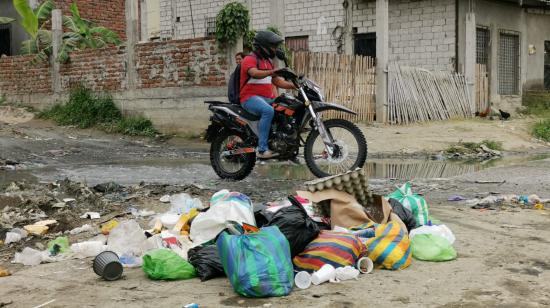 Una motocicleta atraviesa un pozo de aguas servidas donde se acumula un montículo de basura en la cooperativa San Francisco, al norte de Guayaquil, territorio del grupo criminal Los Lobos.