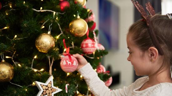 Imagen referencial de una niña junto a un árbol de Navidad.