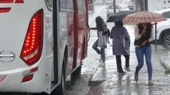 Personas con paraguas en una parada de bus de Cuenca, se cubren de la lluvia.